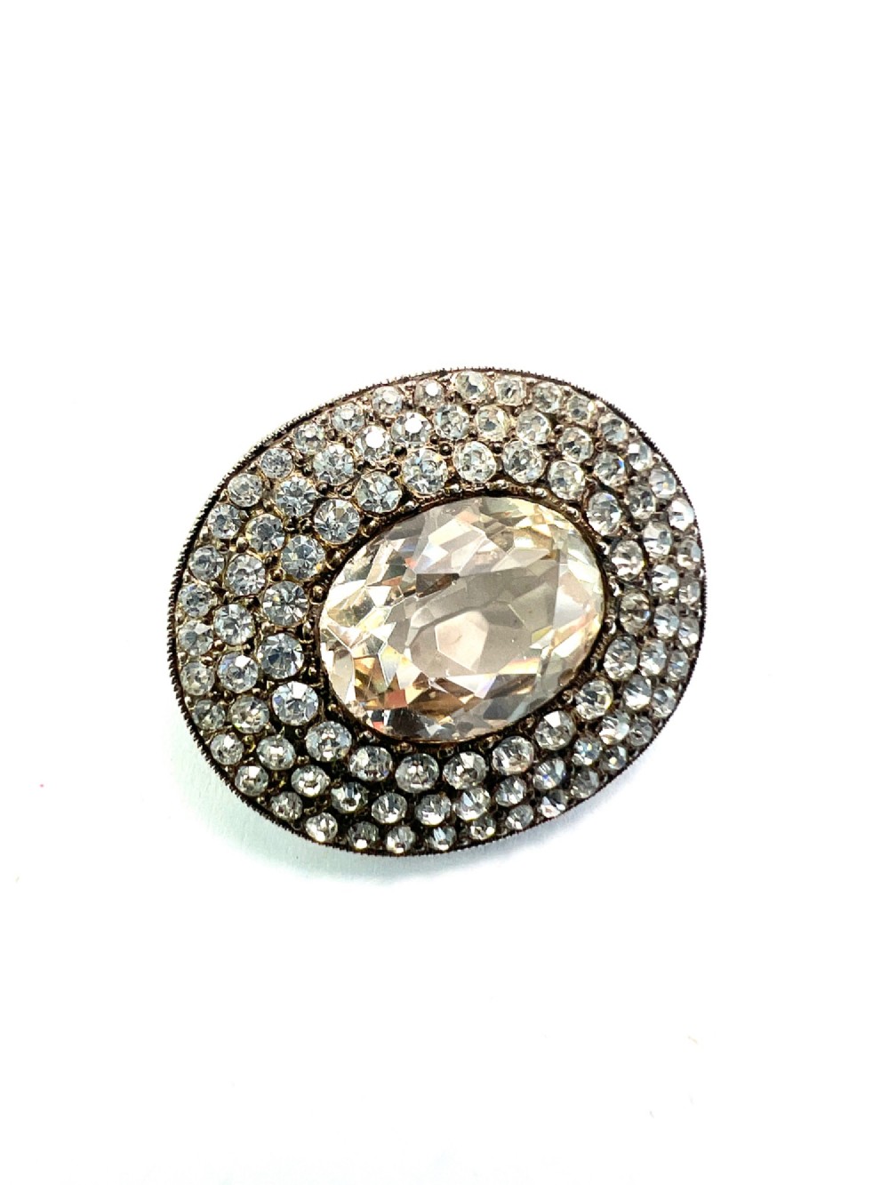 An oval Edwardian brooch featuring a large central oval paste stone bordered by multiple rows of smaller brilliant-cut paste stones in a silver mounting. View II