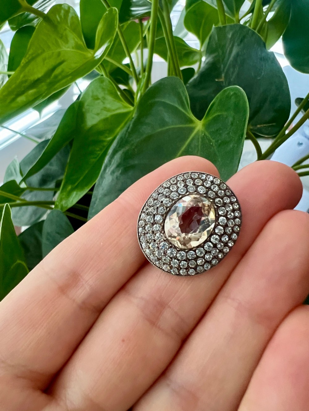 An oval Edwardian brooch featuring a large central oval paste stone bordered by multiple rows of smaller brilliant-cut paste stones in a silver mounting. View VIII