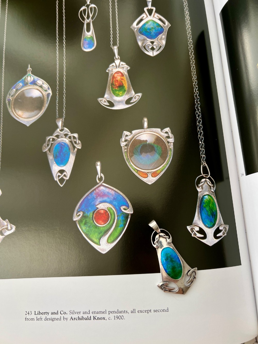 A silver Arts and Crafts style openwork pendant featuring stylised Celtic knots around a central oval blue and green enamel insert. View VI