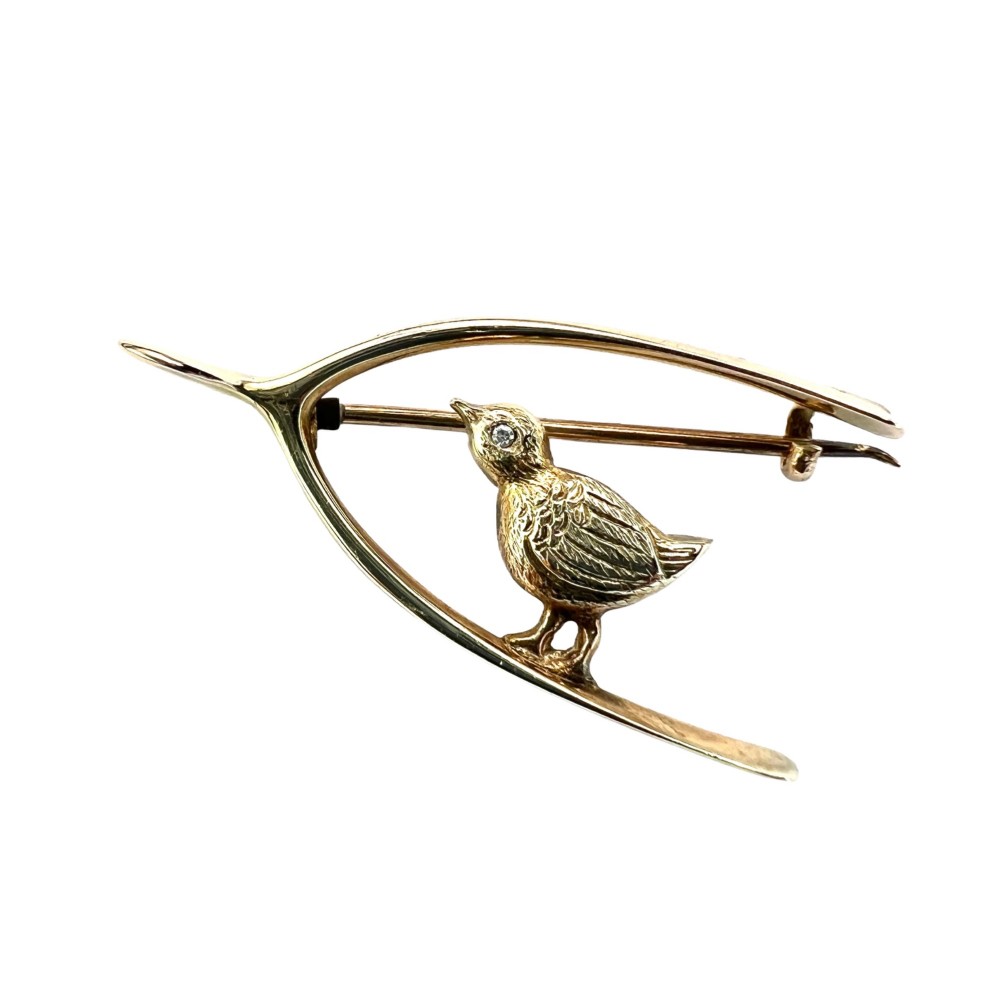 An Edwardian 9ct gold wishbone brooch featuring an engraved chick with a small diamond eye.