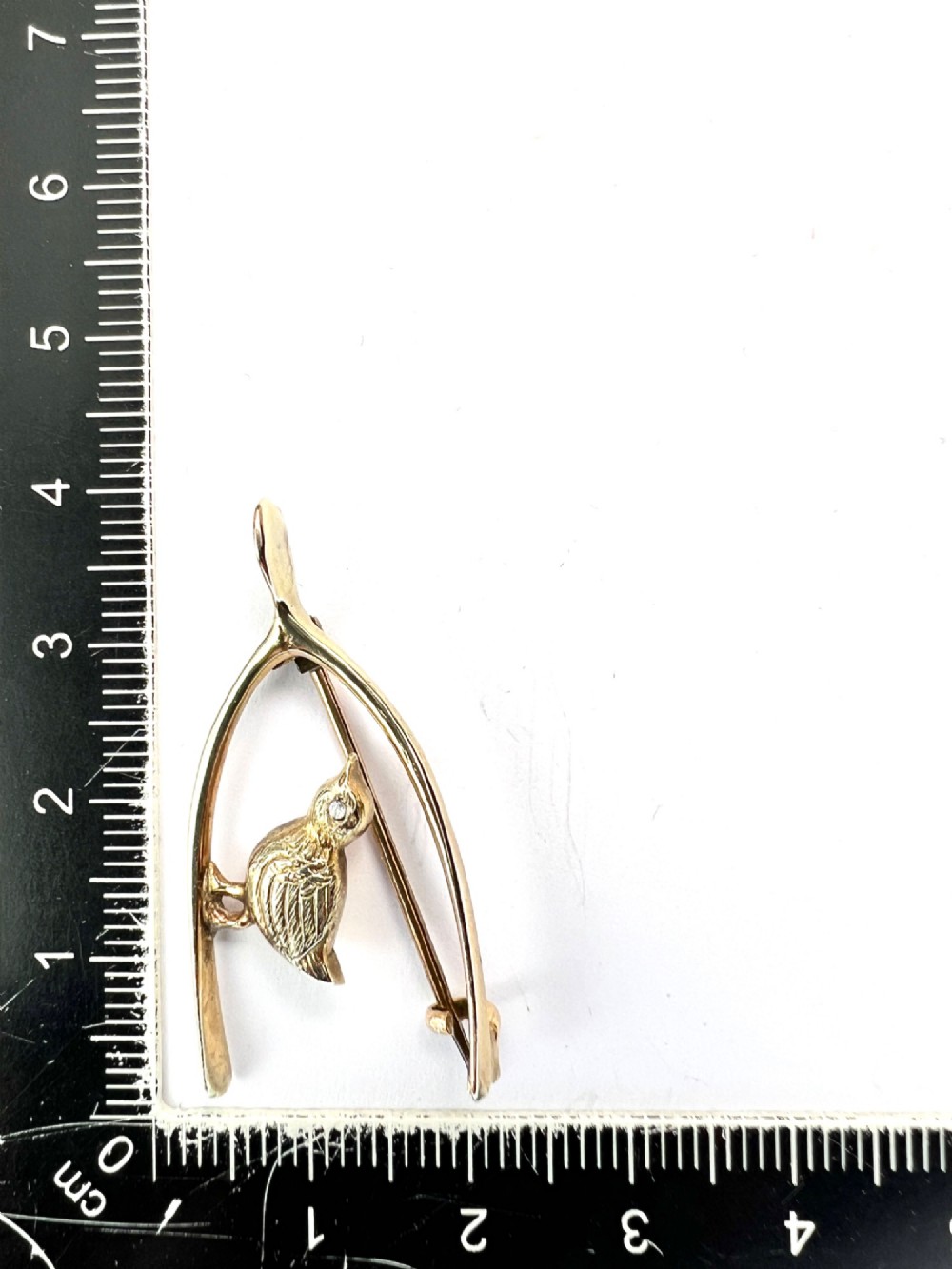 An Edwardian 9ct gold wishbone brooch featuring an engraved chick with a small diamond eye. View II