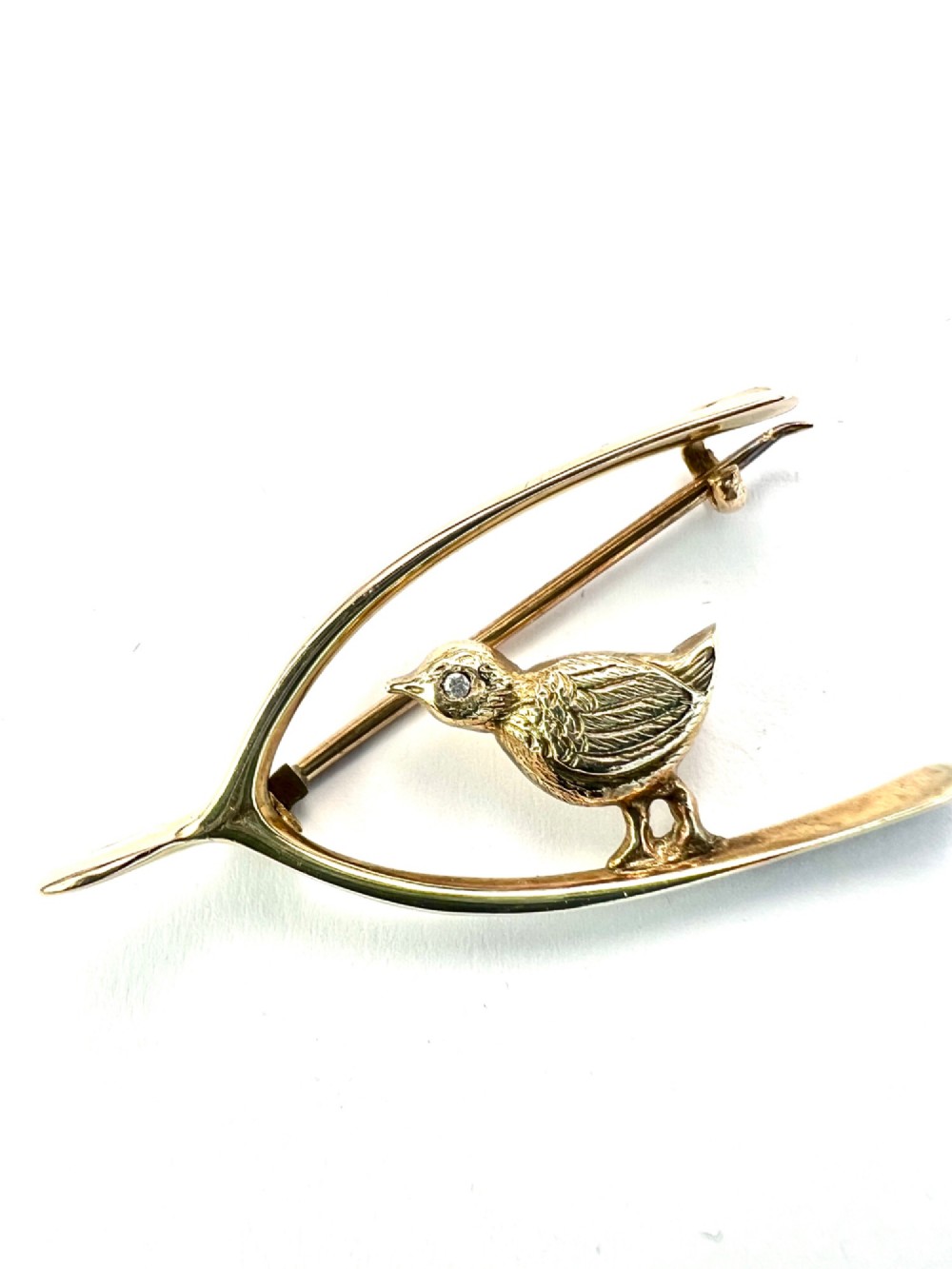 An Edwardian 9ct gold wishbone brooch featuring an engraved chick with a small diamond eye. View V