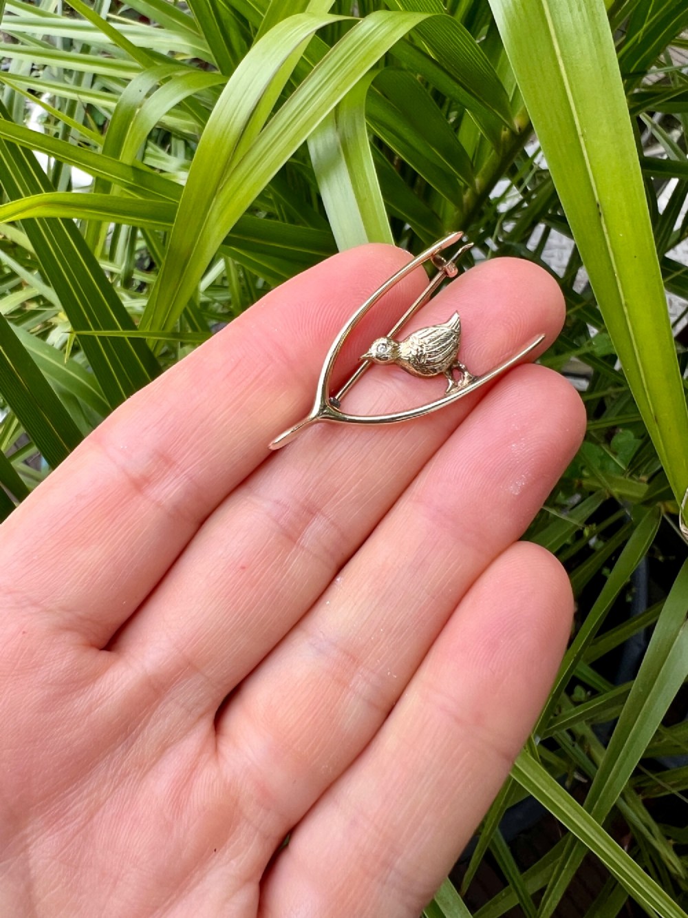 An Edwardian 9ct gold wishbone brooch featuring an engraved chick with a small diamond eye. View VI