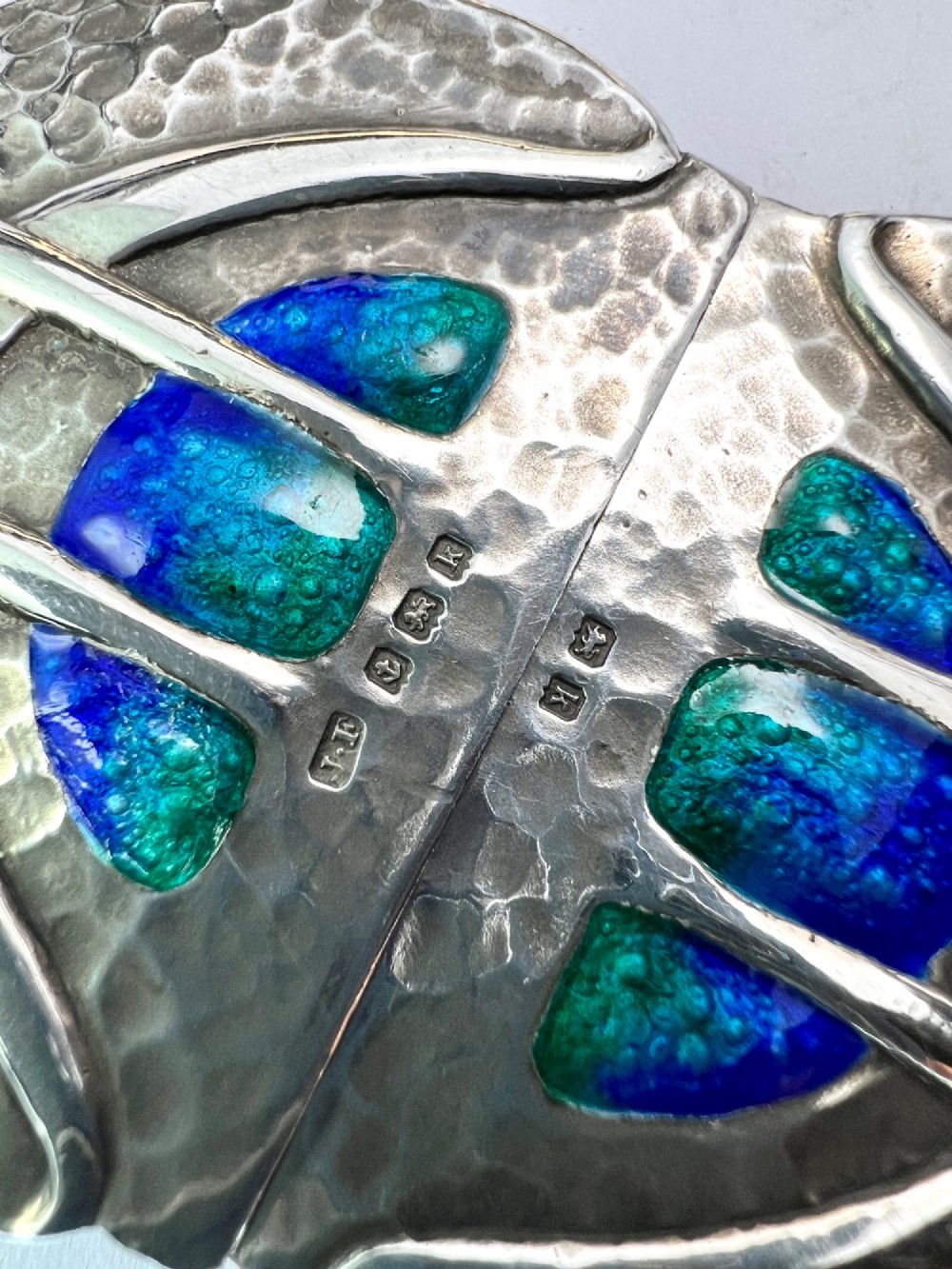 A two-part Art Nouveau sterling silver belt buckle featuring hand-hammered oval surfaces inlaid with vibrant blue and green enamelling and hallmarked in the centre. View V