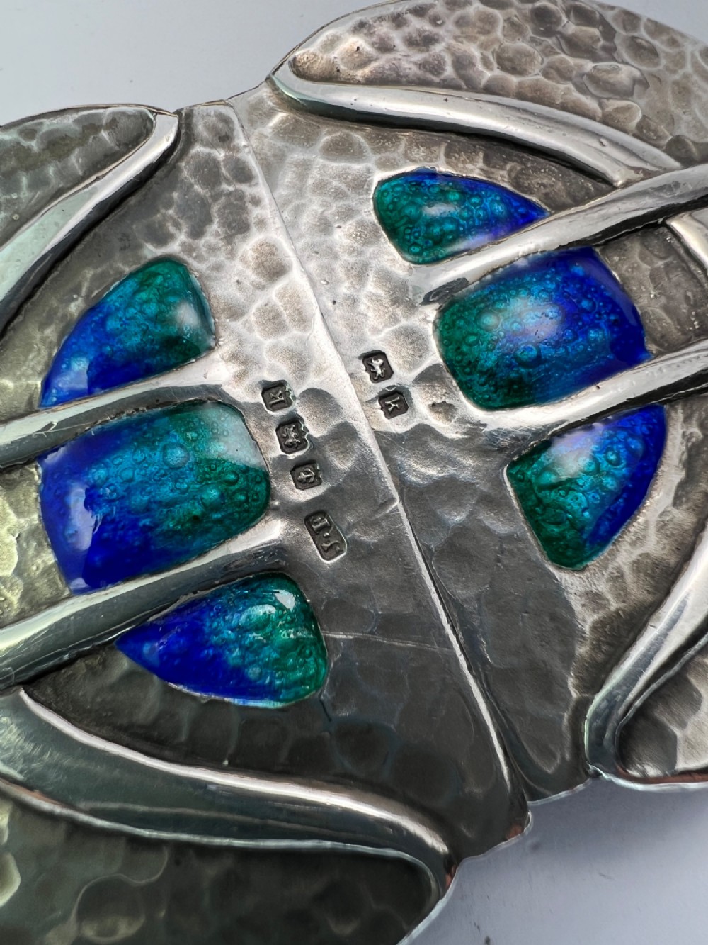A two-part Art Nouveau sterling silver belt buckle featuring hand-hammered oval surfaces inlaid with vibrant blue and green enamelling and hallmarked in the centre. View VI