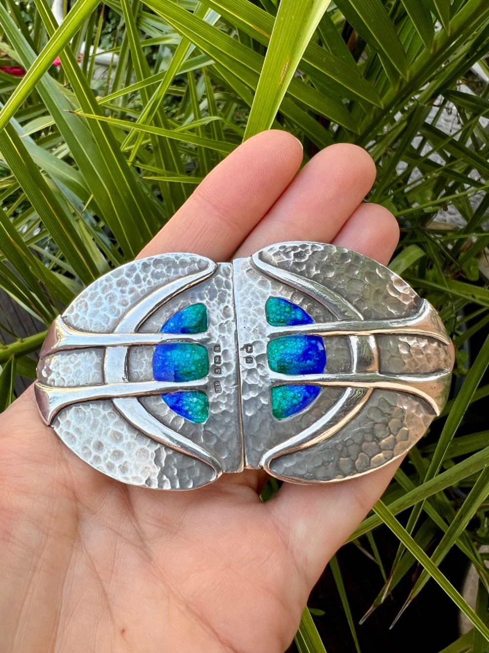 A two-part Art Nouveau sterling silver belt buckle featuring hand-hammered oval surfaces inlaid with vibrant blue and green enamelling and hallmarked in the centre. View X