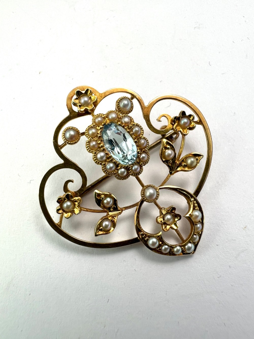 An Edwardian openwork 15ct yellow gold brooch featuring a central oval light blue aquamarine surrounded by seed pearls and floral scroll motifs. View III