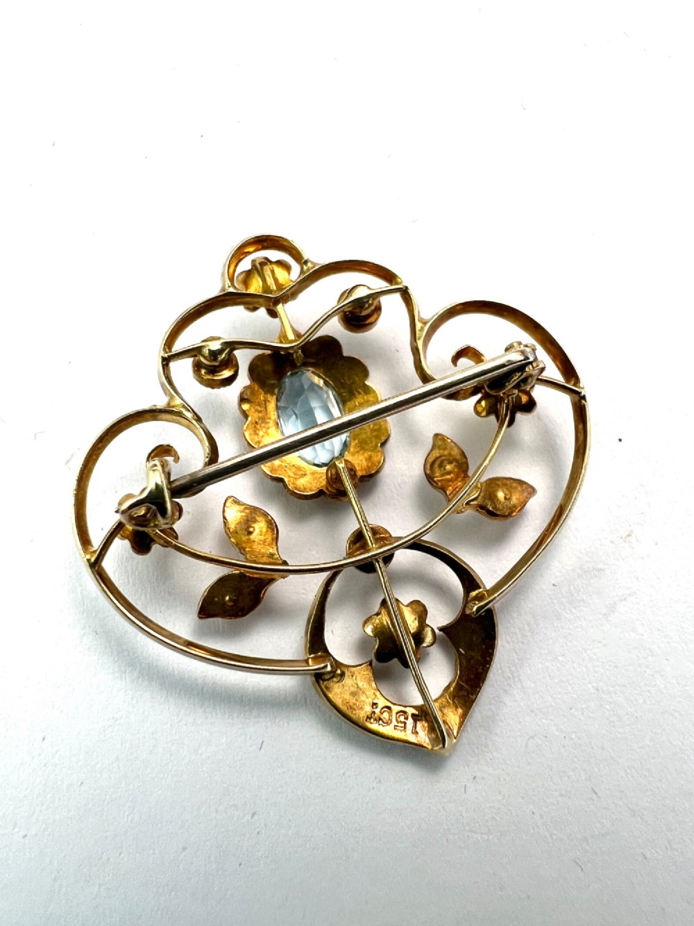 An Edwardian openwork 15ct yellow gold brooch featuring a central oval light blue aquamarine surrounded by seed pearls and floral scroll motifs. View IV