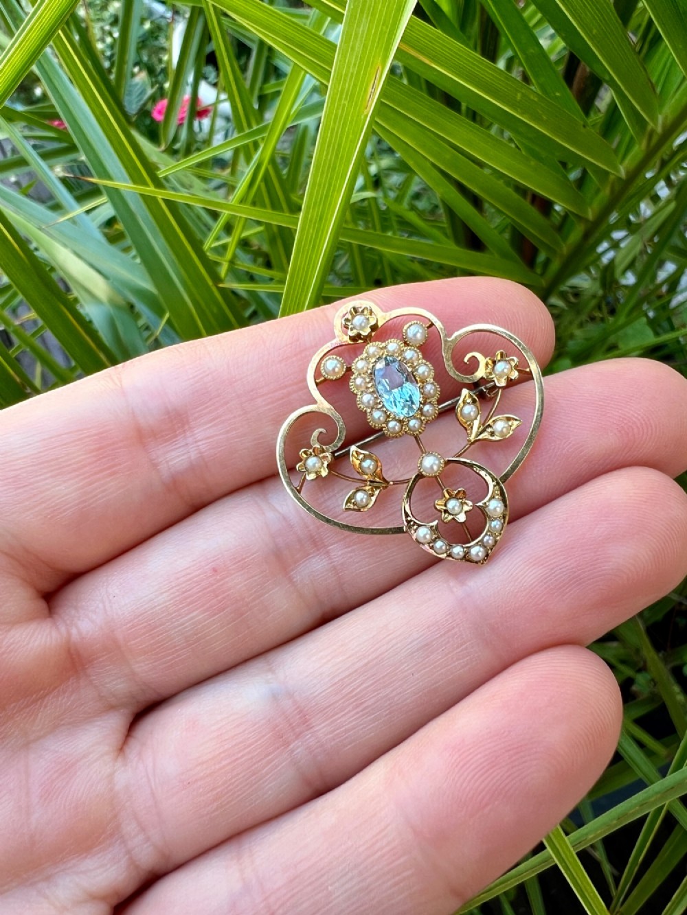 An Edwardian openwork 15ct yellow gold brooch featuring a central oval light blue aquamarine surrounded by seed pearls and floral scroll motifs. View VII