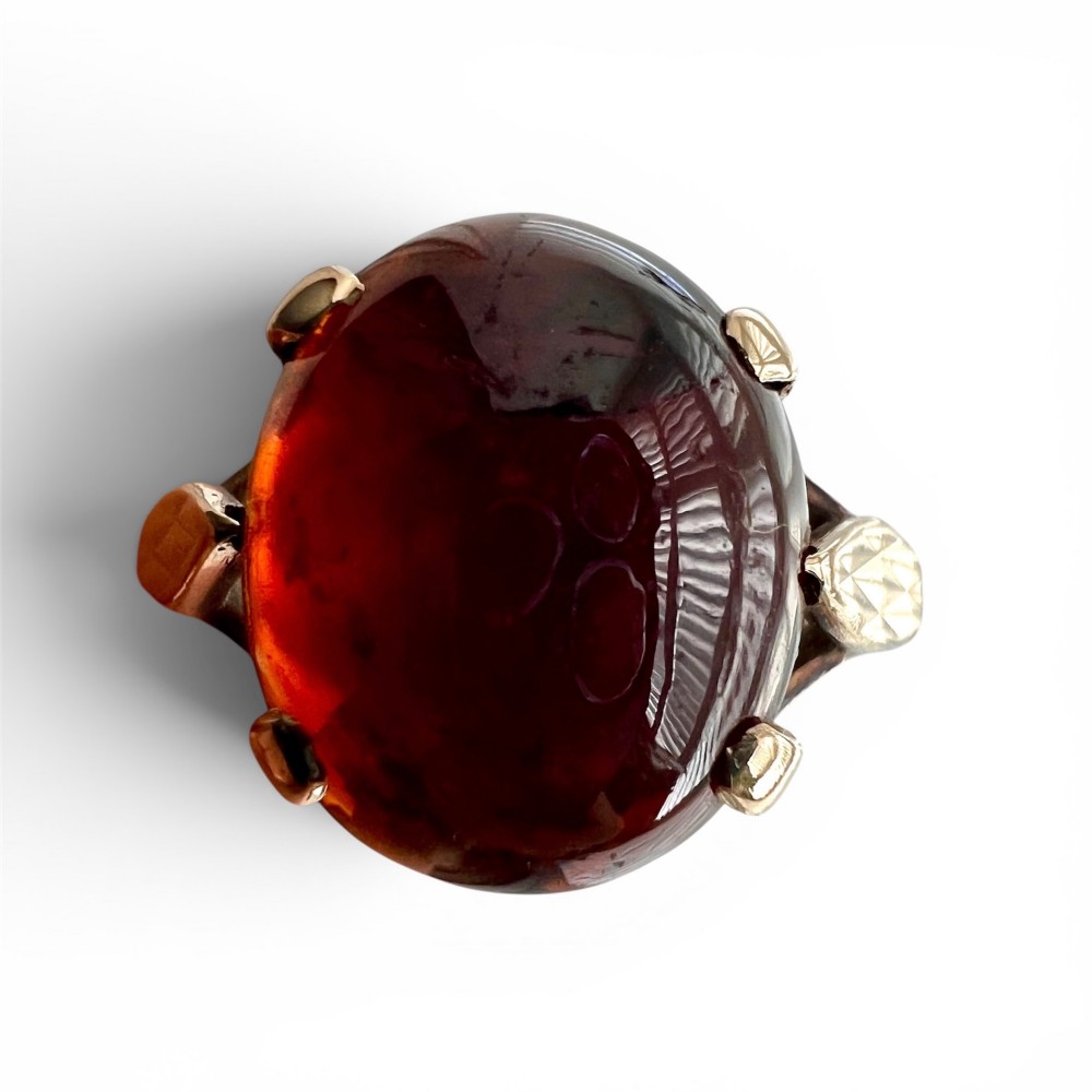An overhead view of a vintage 9ct gold ring featuring a large oval cabochon-cut garnet held by four claw settings.