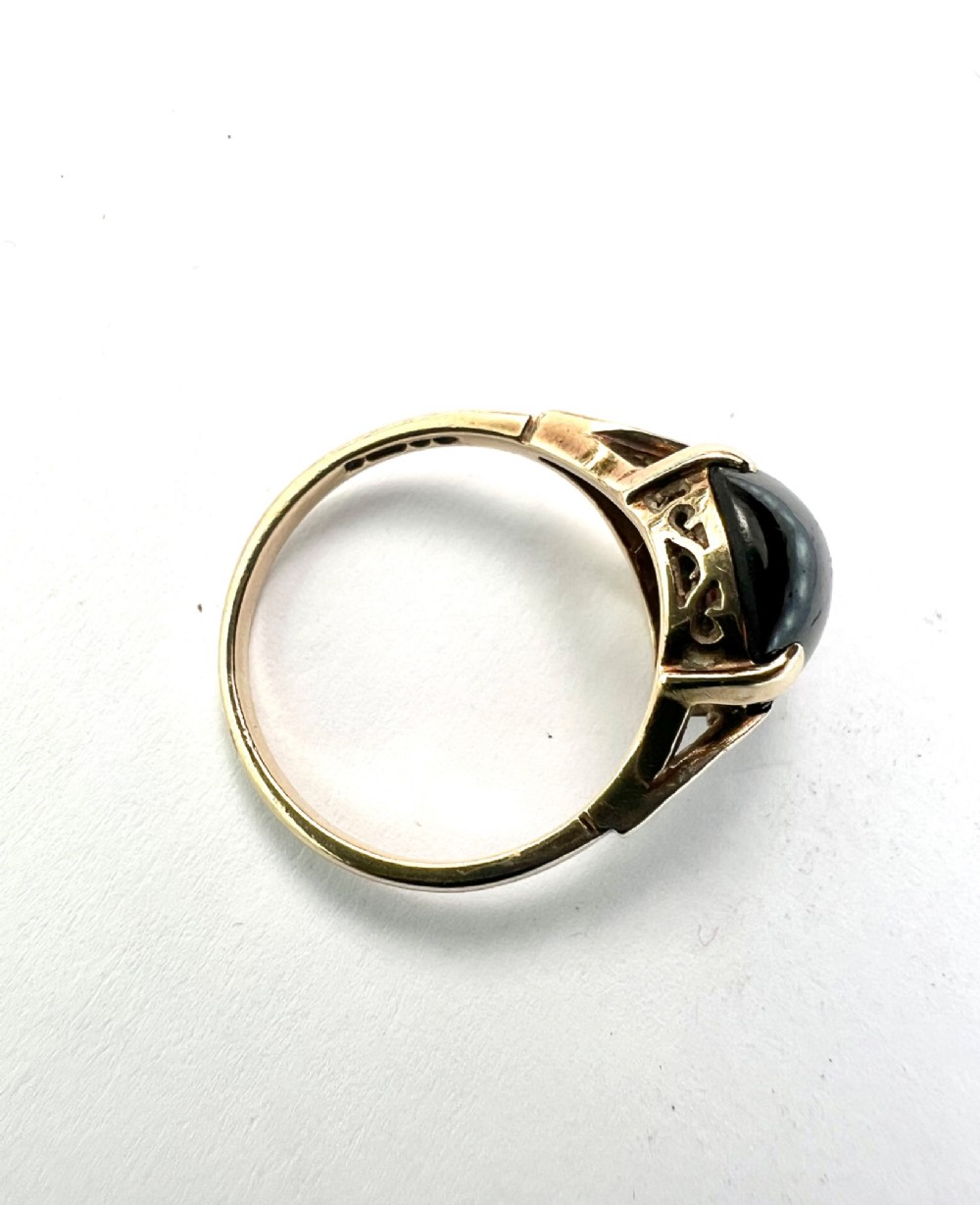 An overhead view of a vintage 9ct gold ring featuring a large oval cabochon-cut garnet held by four claw settings. View V