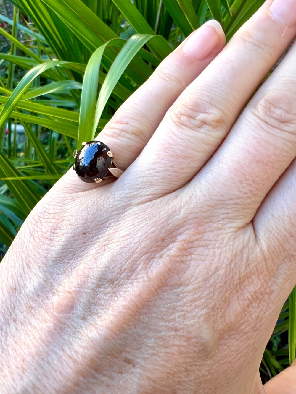 An overhead view of a vintage 9ct gold ring featuring a large oval cabochon-cut garnet held by four claw settings. View VIII