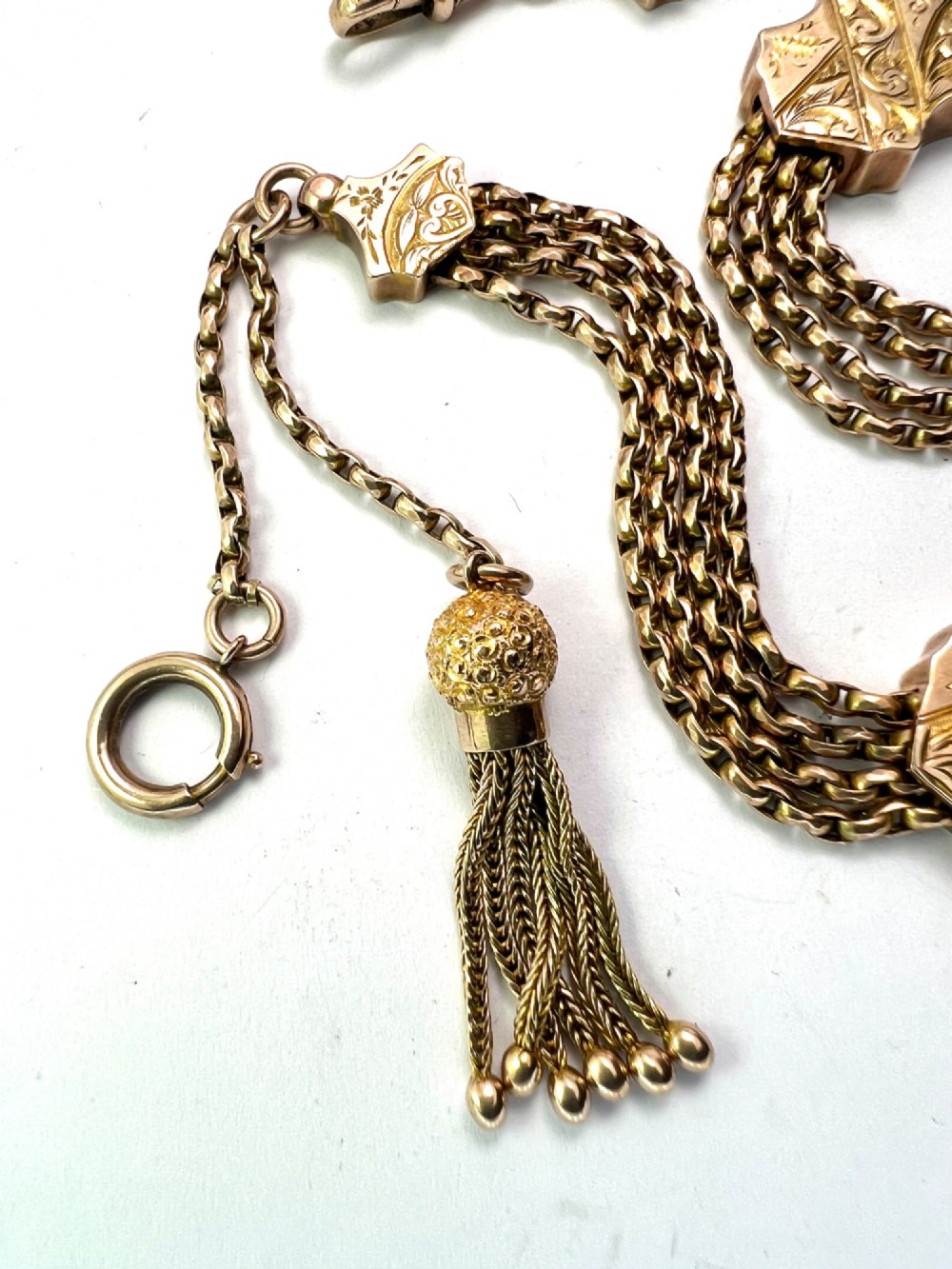 An antique 9ct yellow gold Albertina watch chain featuring four strands, decorative engraved slides, a swivel clasp, and a dangling tassel. View VI