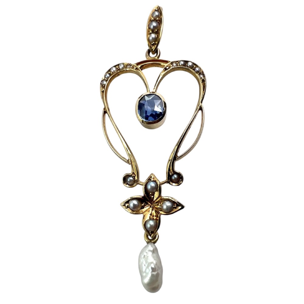 An Art Nouveau 15ct gold openwork lavalier pendant set with seed pearls, a central oval sapphire, and a hanging baroque pearl drop.