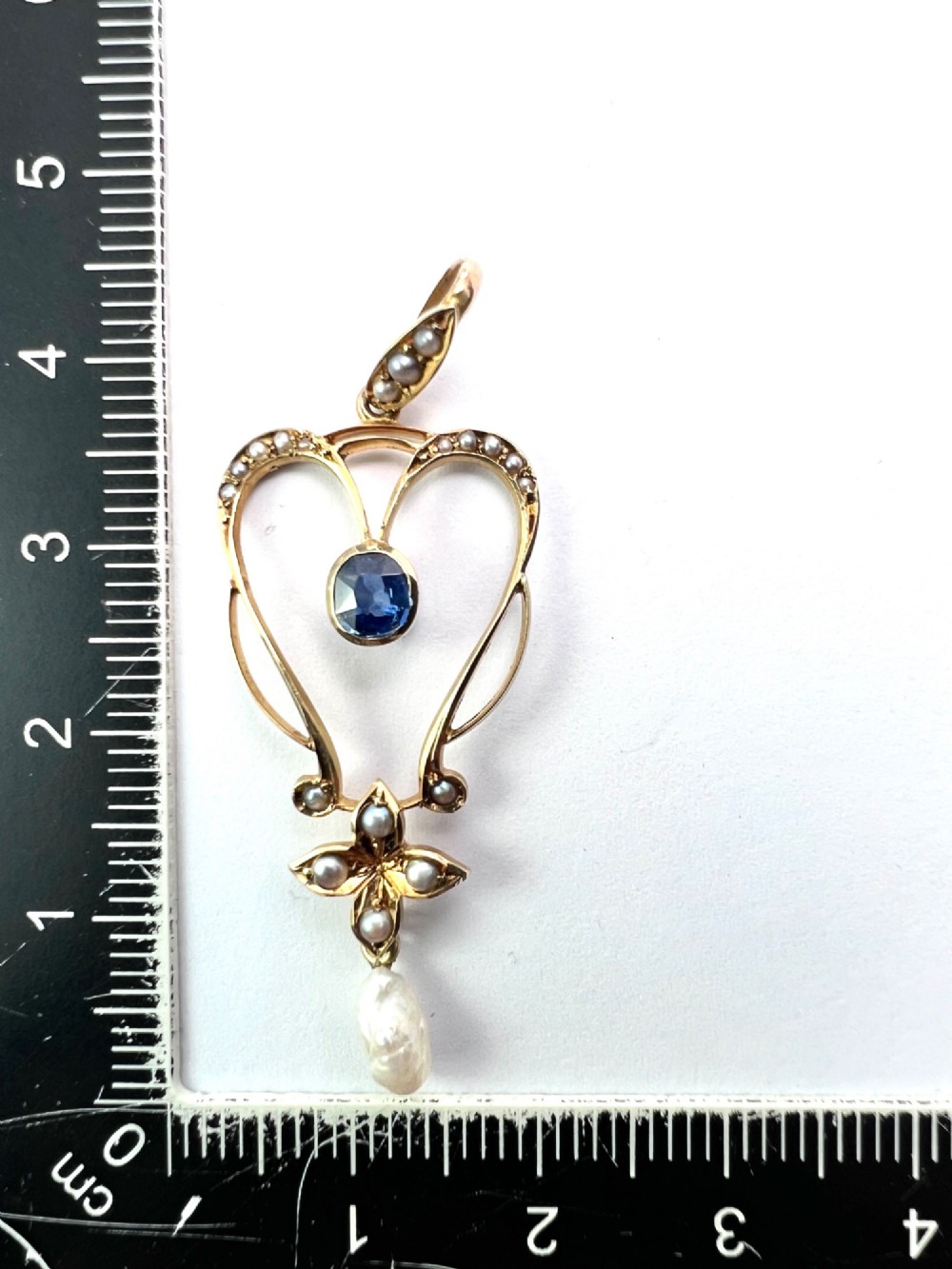 An Art Nouveau 15ct gold openwork lavalier pendant set with seed pearls, a central oval sapphire, and a hanging baroque pearl drop. View II