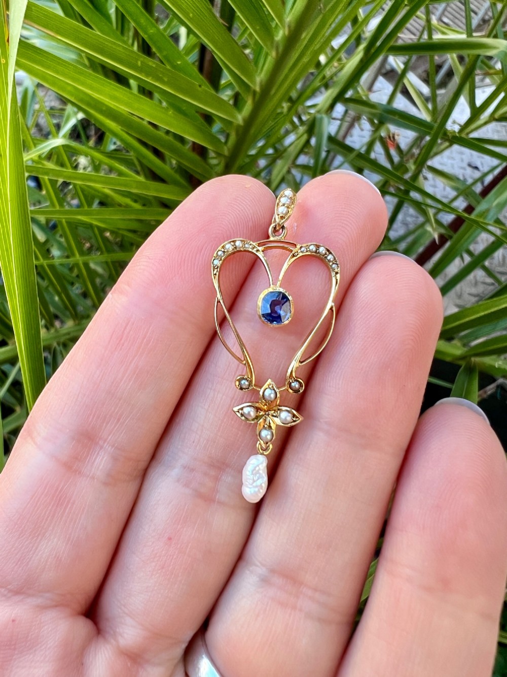 An Art Nouveau 15ct gold openwork lavalier pendant set with seed pearls, a central oval sapphire, and a hanging baroque pearl drop. View IV