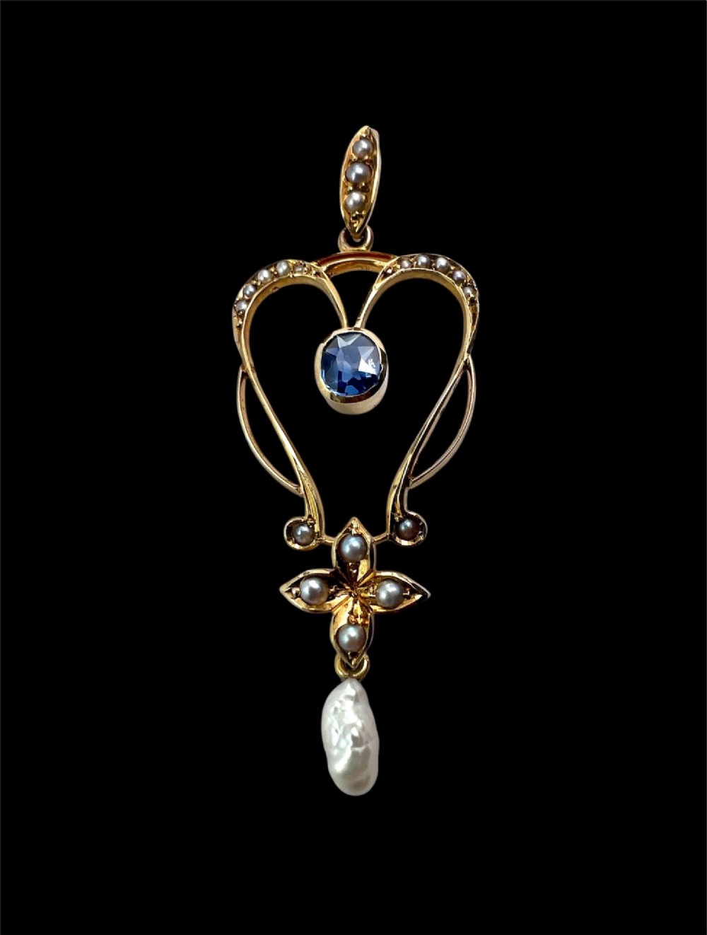 An Art Nouveau 15ct gold openwork lavalier pendant set with seed pearls, a central oval sapphire, and a hanging baroque pearl drop. View V