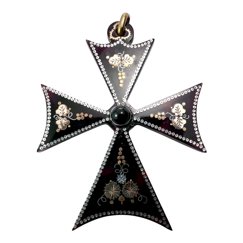 A dark tortoiseshell cross pattee pendant decorated with gold and silver pique inlay of foliate motifs and bordered by silver pinwork with a central black cabochon.