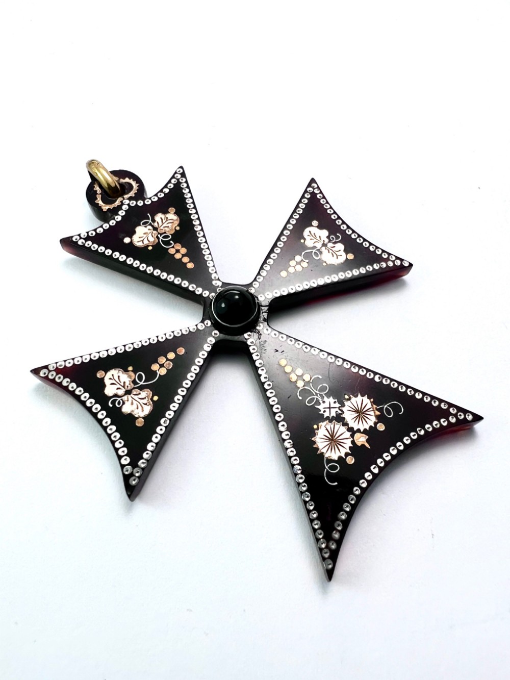 A dark tortoiseshell cross pattee pendant decorated with gold and silver pique inlay of foliate motifs and bordered by silver pinwork with a central black cabochon. View II