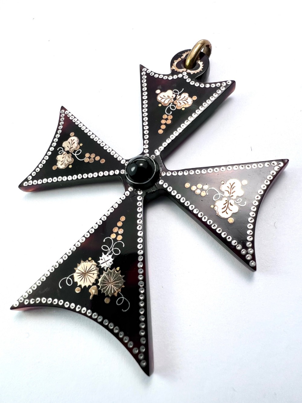 A dark tortoiseshell cross pattee pendant decorated with gold and silver pique inlay of foliate motifs and bordered by silver pinwork with a central black cabochon. View III