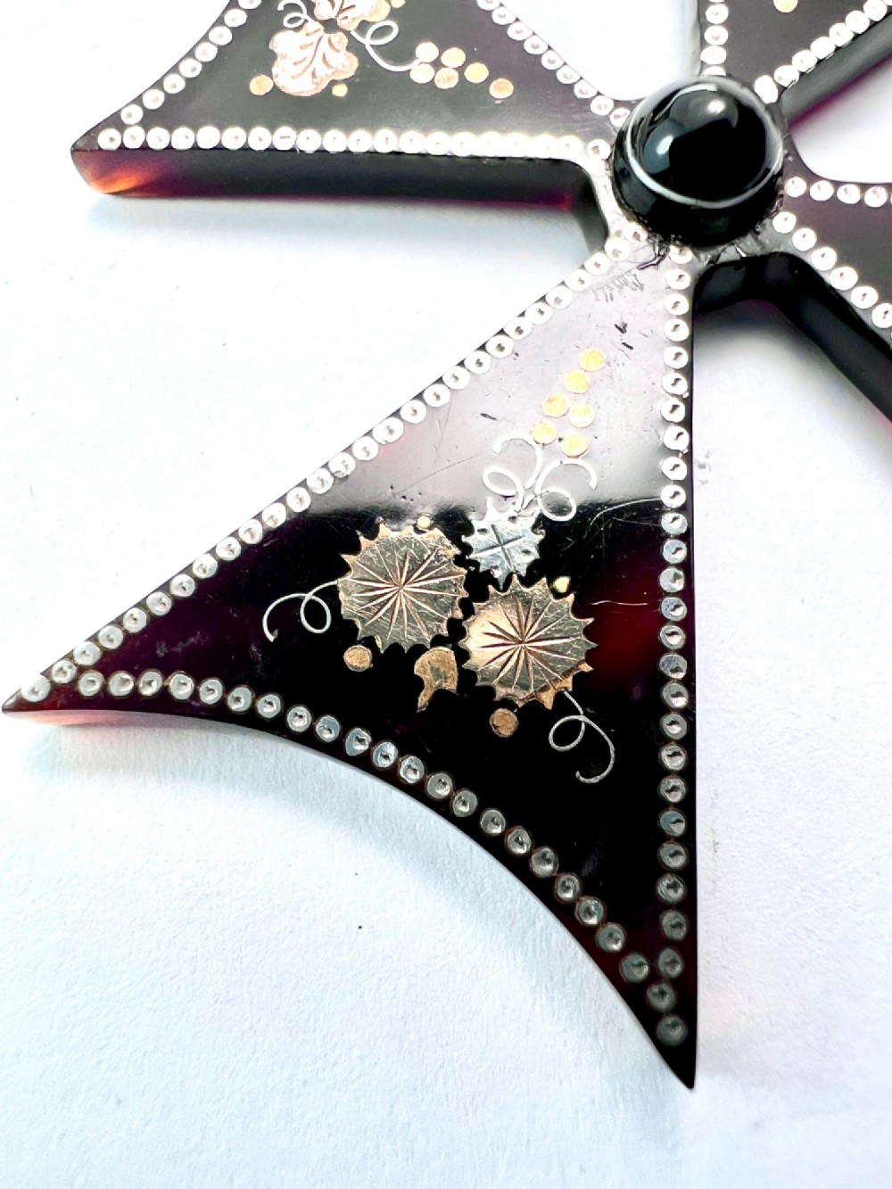 A dark tortoiseshell cross pattee pendant decorated with gold and silver pique inlay of foliate motifs and bordered by silver pinwork with a central black cabochon. View V