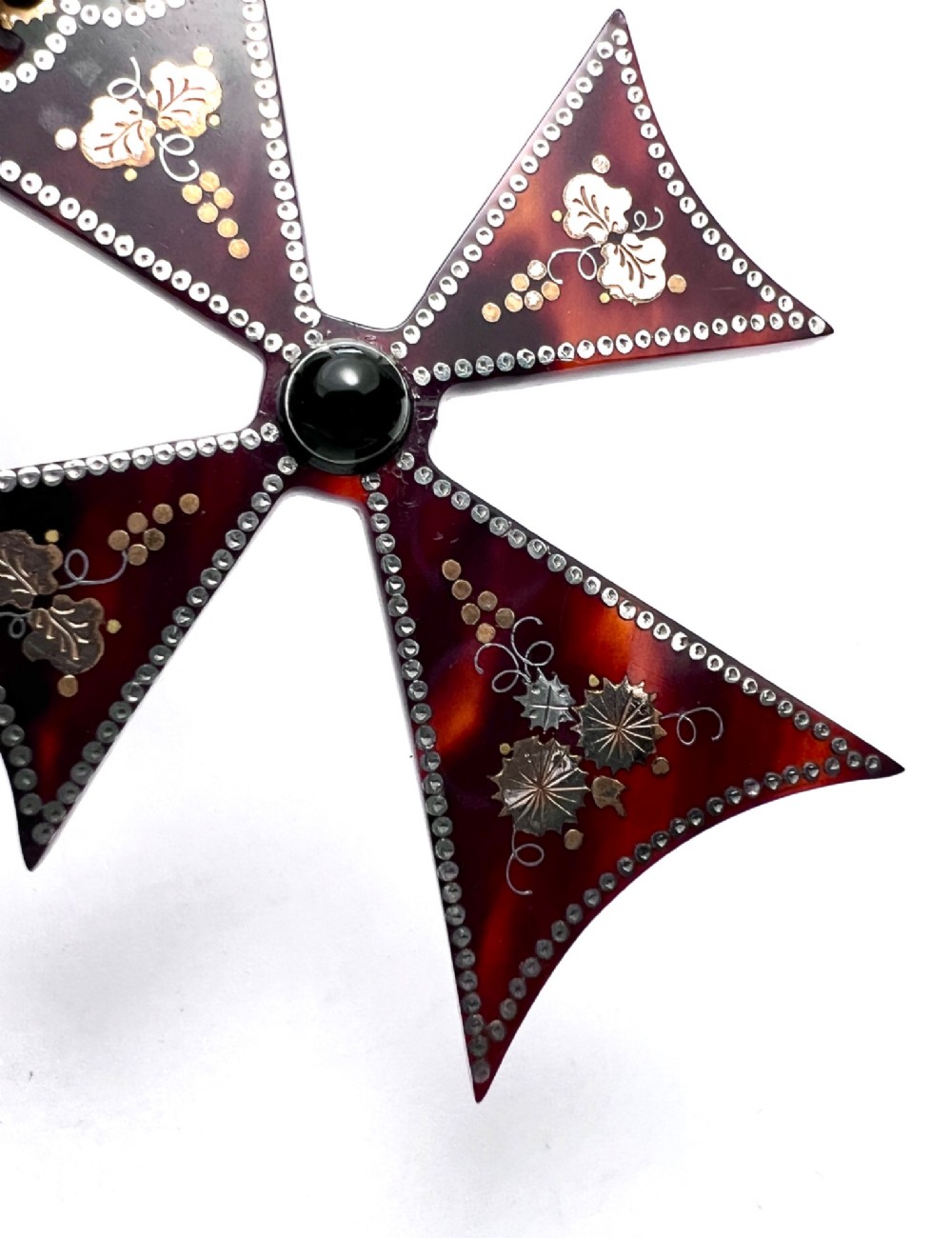 A dark tortoiseshell cross pattee pendant decorated with gold and silver pique inlay of foliate motifs and bordered by silver pinwork with a central black cabochon. View VI