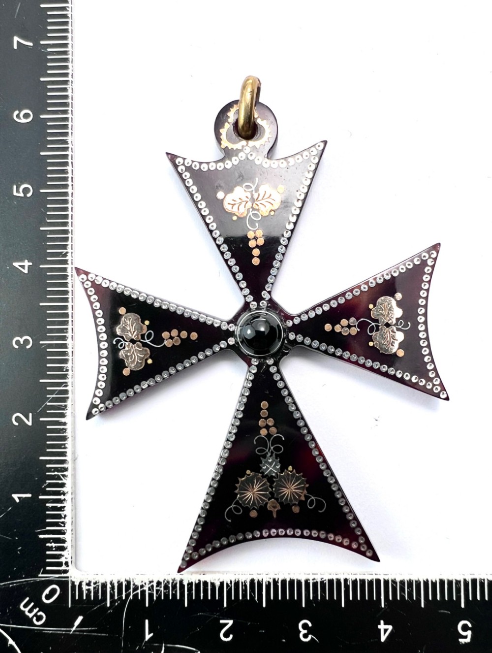 A dark tortoiseshell cross pattee pendant decorated with gold and silver pique inlay of foliate motifs and bordered by silver pinwork with a central black cabochon. View VII
