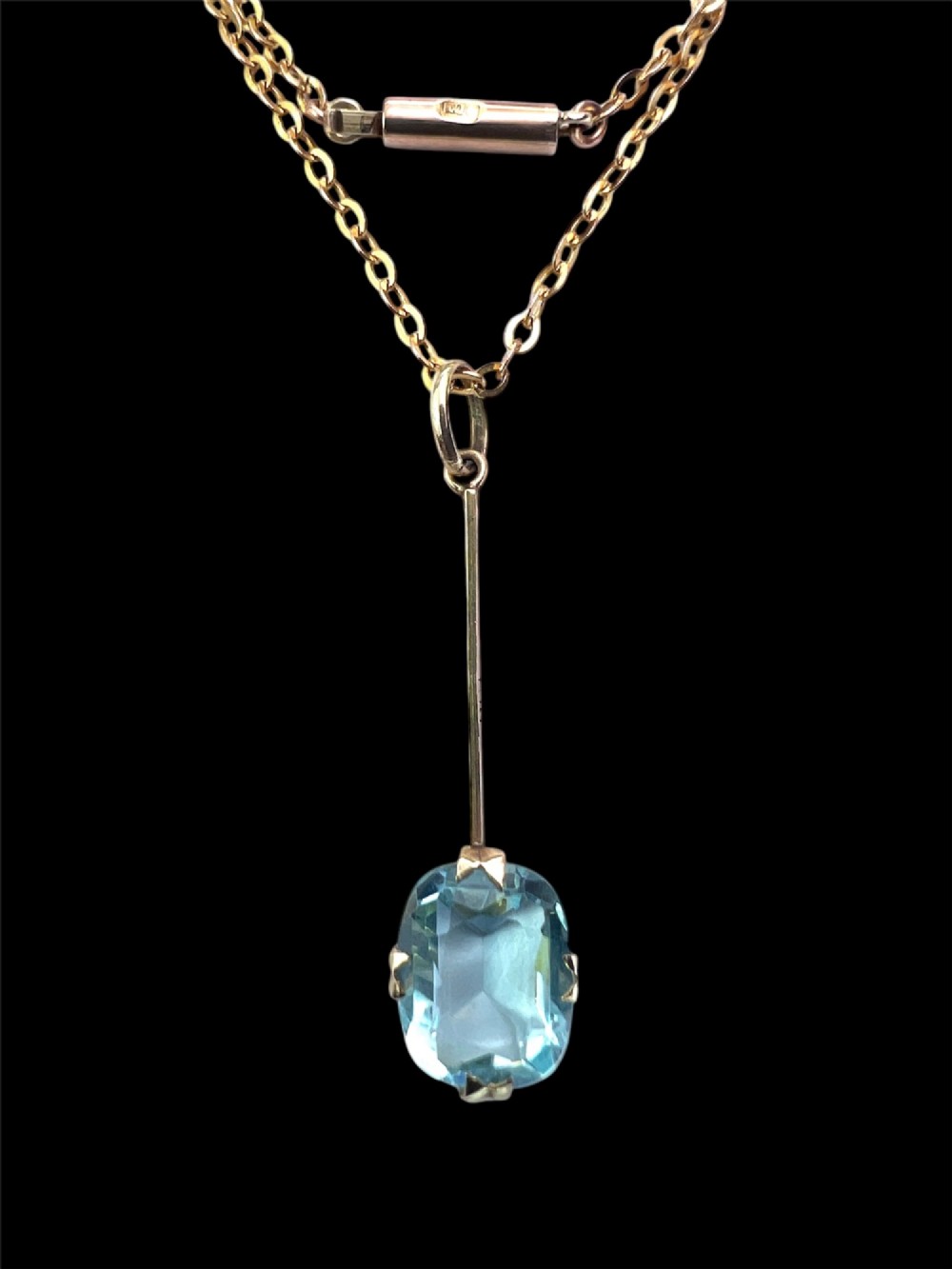 An Edwardian 9ct gold fine chain necklace featuring a linear bar drop suspending a blue paste aquamarine gemstone. View II