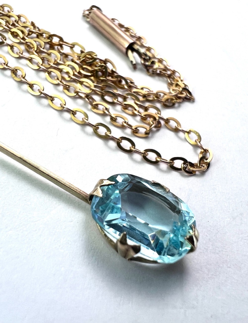 An Edwardian 9ct gold fine chain necklace featuring a linear bar drop suspending a blue paste aquamarine gemstone. View VI