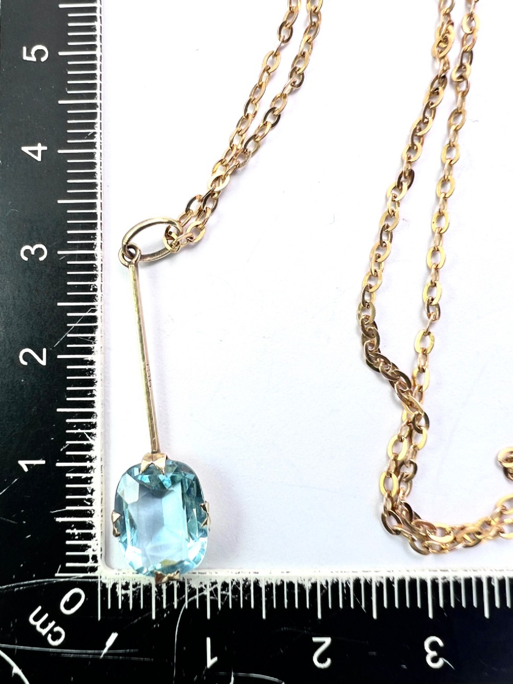 An Edwardian 9ct gold fine chain necklace featuring a linear bar drop suspending a blue paste aquamarine gemstone. View VII