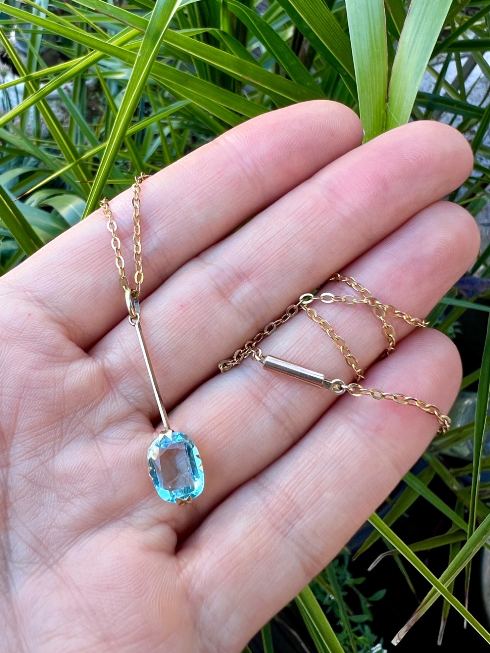 An Edwardian 9ct gold fine chain necklace featuring a linear bar drop suspending a blue paste aquamarine gemstone. View VIII