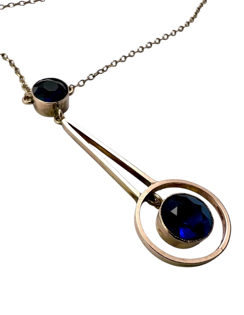 An Edwardian 9ct gold fine chain necklace featuring a geometric drop pendant set with two faceted dark blue paste stones. View III
