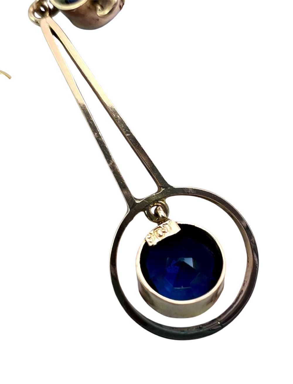 An Edwardian 9ct gold fine chain necklace featuring a geometric drop pendant set with two faceted dark blue paste stones. View V