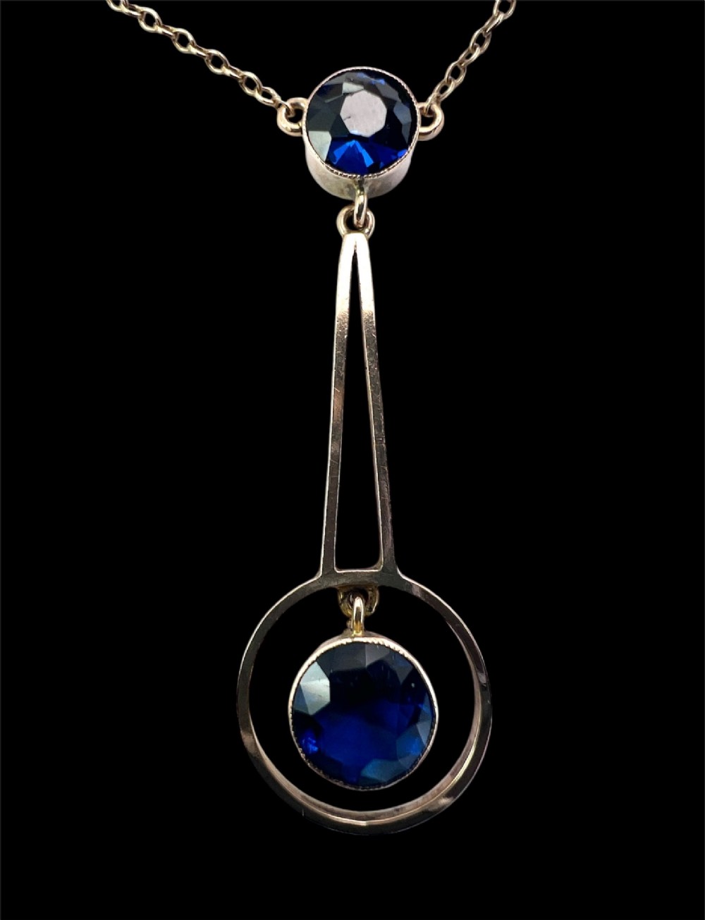 An Edwardian 9ct gold fine chain necklace featuring a geometric drop pendant set with two faceted dark blue paste stones. View VI