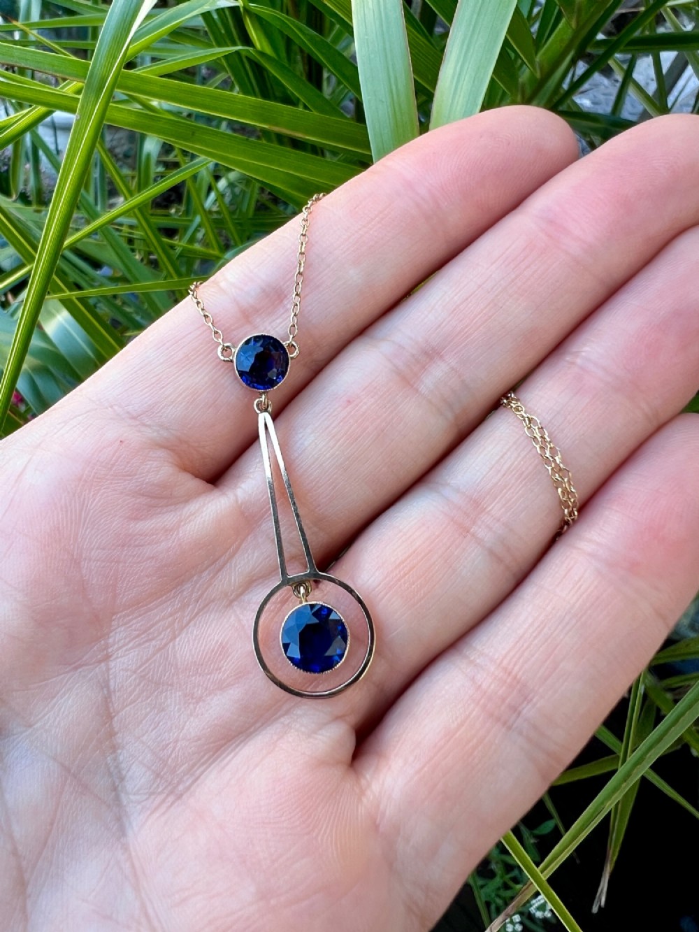 An Edwardian 9ct gold fine chain necklace featuring a geometric drop pendant set with two faceted dark blue paste stones. View VII
