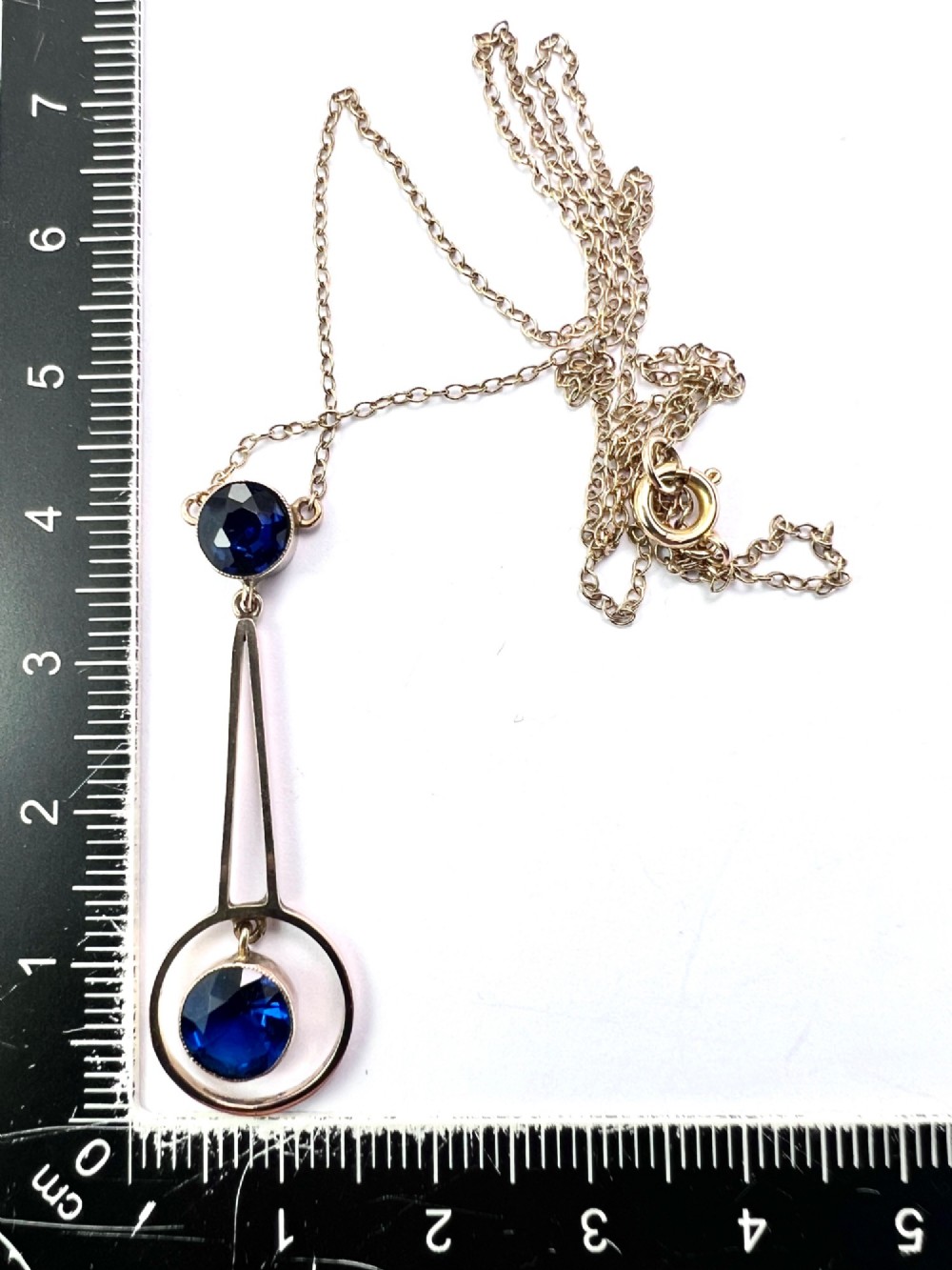 An Edwardian 9ct gold fine chain necklace featuring a geometric drop pendant set with two faceted dark blue paste stones. View IX