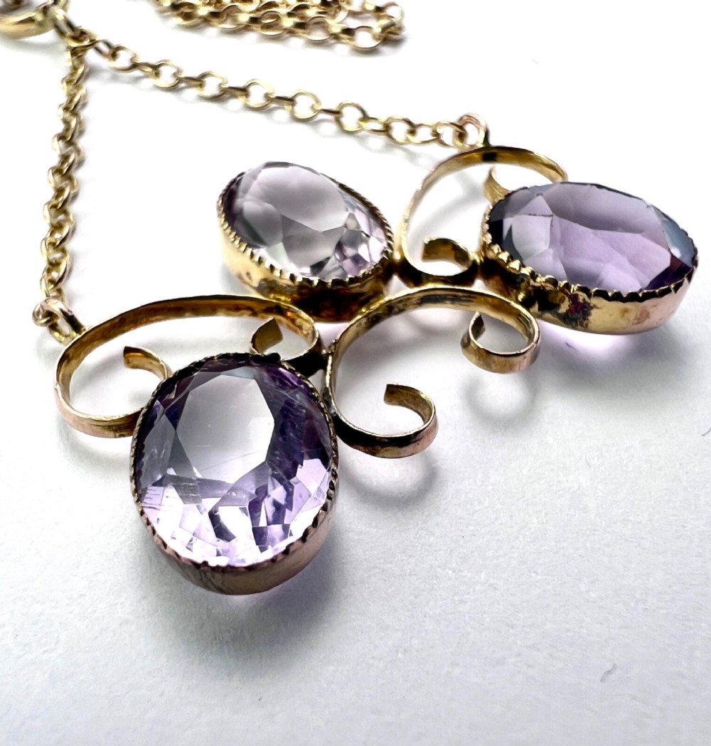 An Edwardian 9ct gold pendant necklace featuring three oval facet-cut purple amethysts set within openwork gold scrollwork. View V