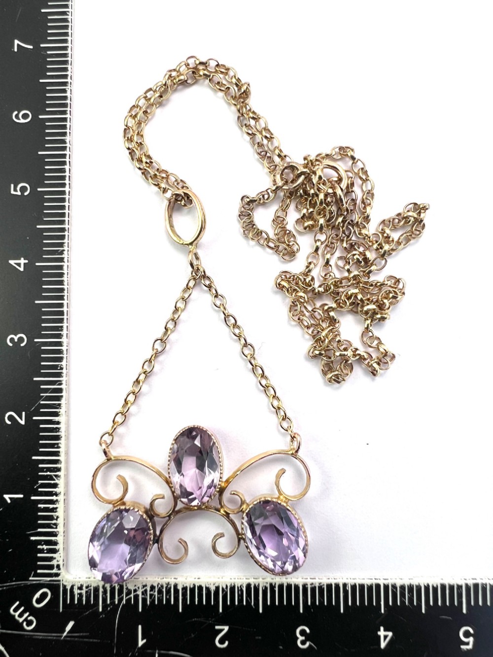 An Edwardian 9ct gold pendant necklace featuring three oval facet-cut purple amethysts set within openwork gold scrollwork. View VI