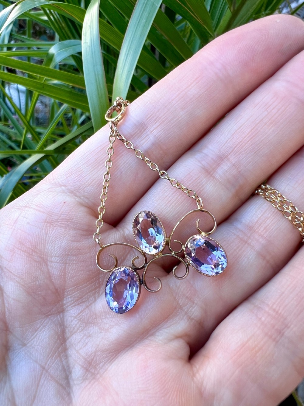 An Edwardian 9ct gold pendant necklace featuring three oval facet-cut purple amethysts set within openwork gold scrollwork. View VII