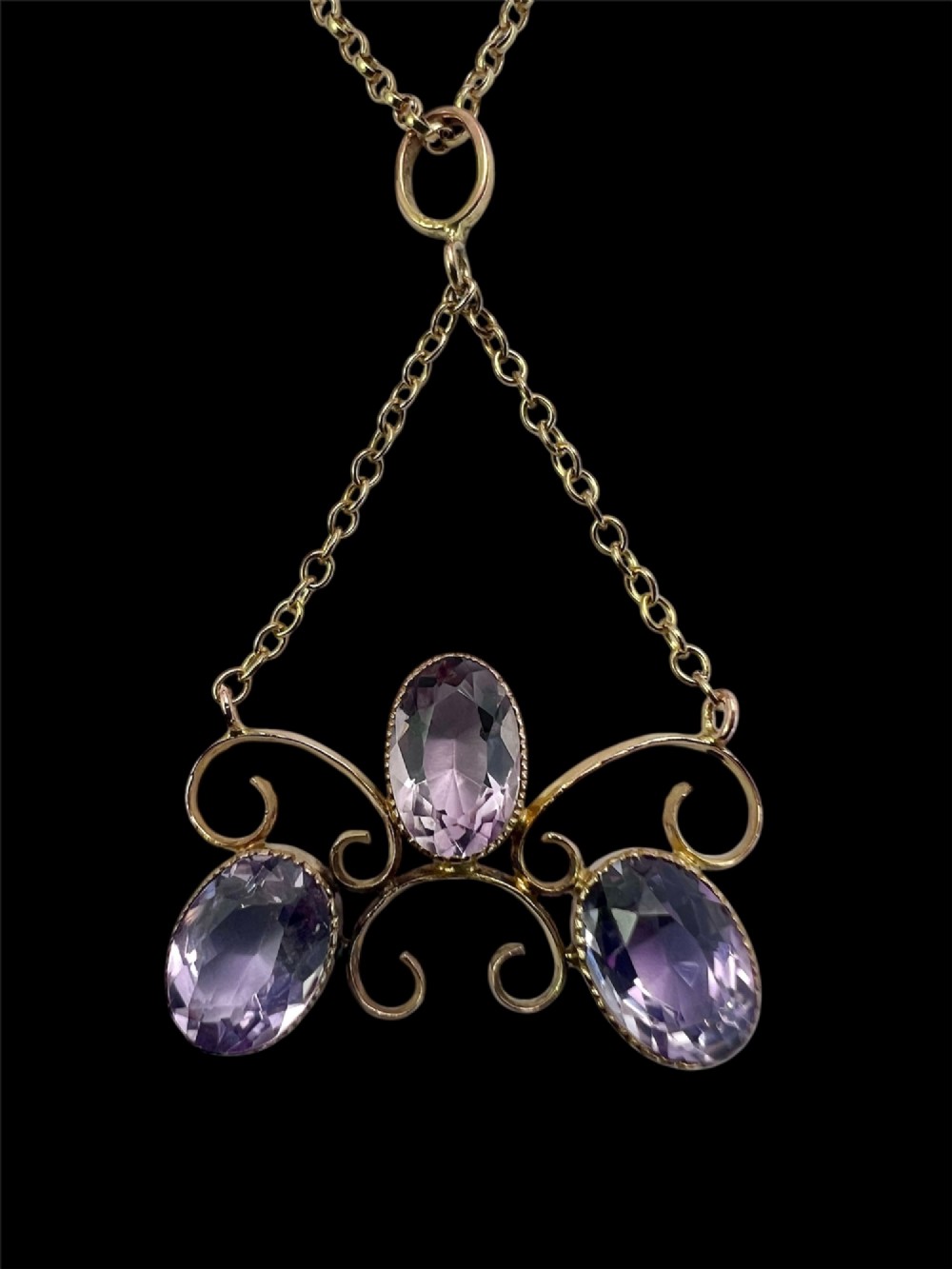An Edwardian 9ct gold pendant necklace featuring three oval facet-cut purple amethysts set within openwork gold scrollwork. View VIII