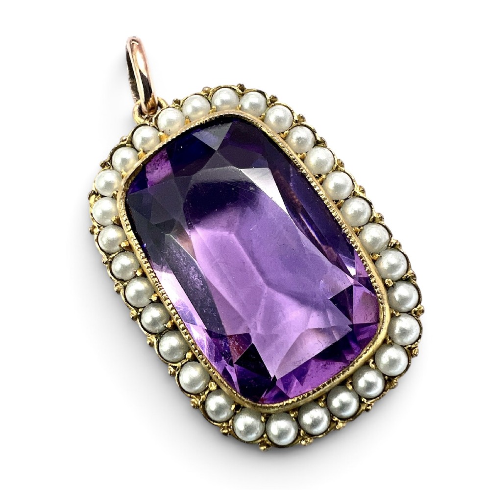 A Victorian rectangular cushion-cut purple paste stone pendant surrounded by a halo of small white seed pearls in a gold mount.