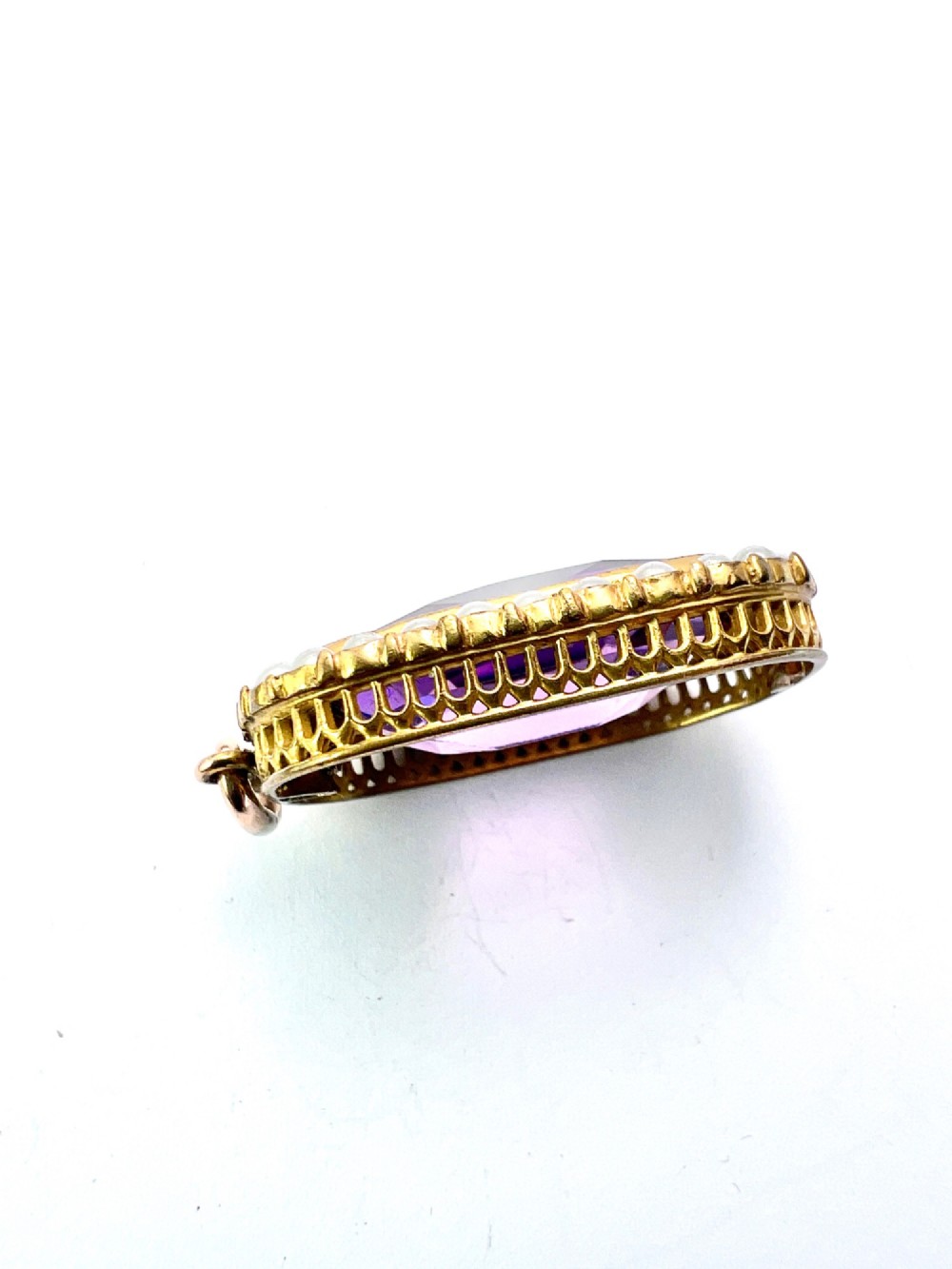 A Victorian rectangular cushion-cut purple paste stone pendant surrounded by a halo of small white seed pearls in a gold mount. View V