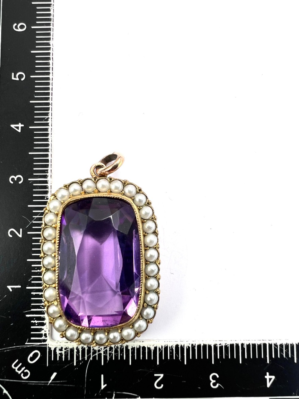 A Victorian rectangular cushion-cut purple paste stone pendant surrounded by a halo of small white seed pearls in a gold mount. View VI