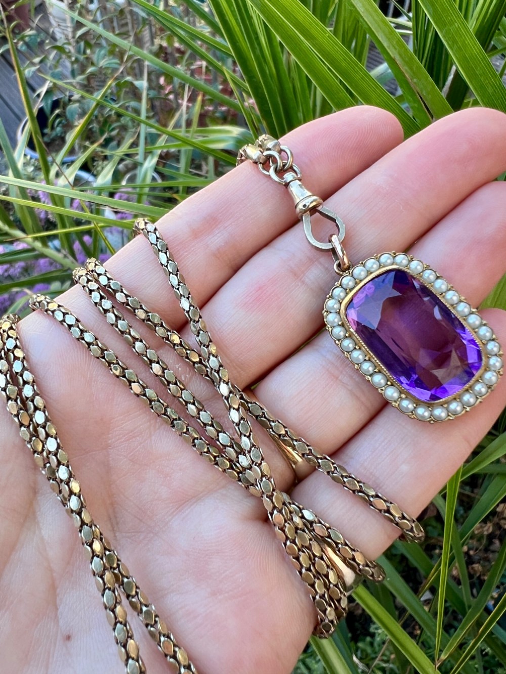 A Victorian rectangular cushion-cut purple paste stone pendant surrounded by a halo of small white seed pearls in a gold mount. View X