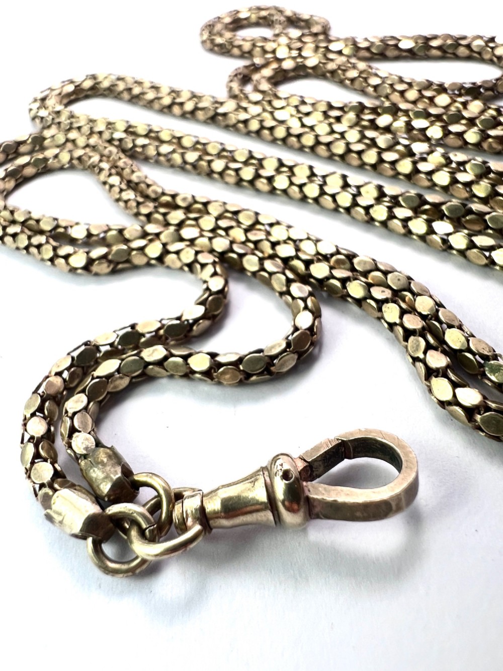 A long yellow gold longuard chain featuring faceted textured links and an Albert swivel clip at the end on a white surface. View II