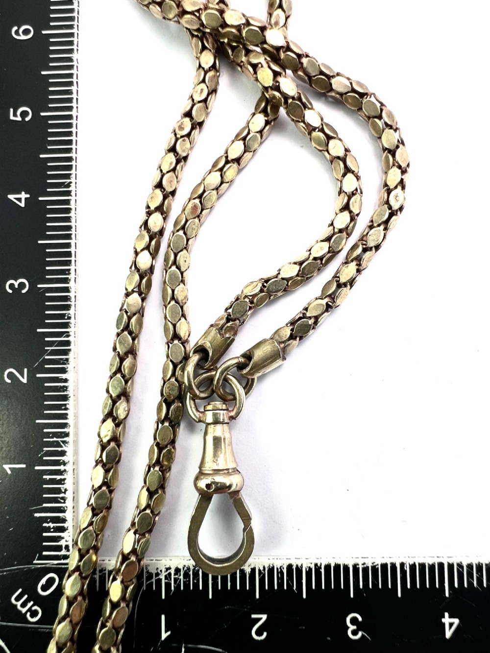 A long yellow gold longuard chain featuring faceted textured links and an Albert swivel clip at the end on a white surface. View IV