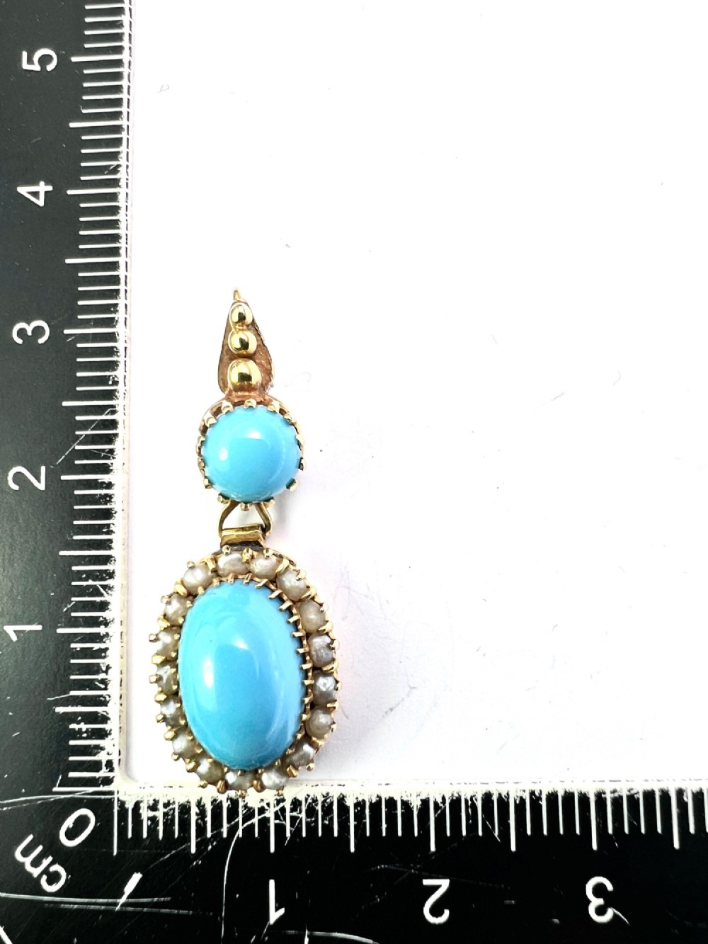 A Victorian yellow gold drop pendant featuring an oval turquoise cabochon framed by a seed pearl halo, hanging below a smaller round turquoise stone. View V