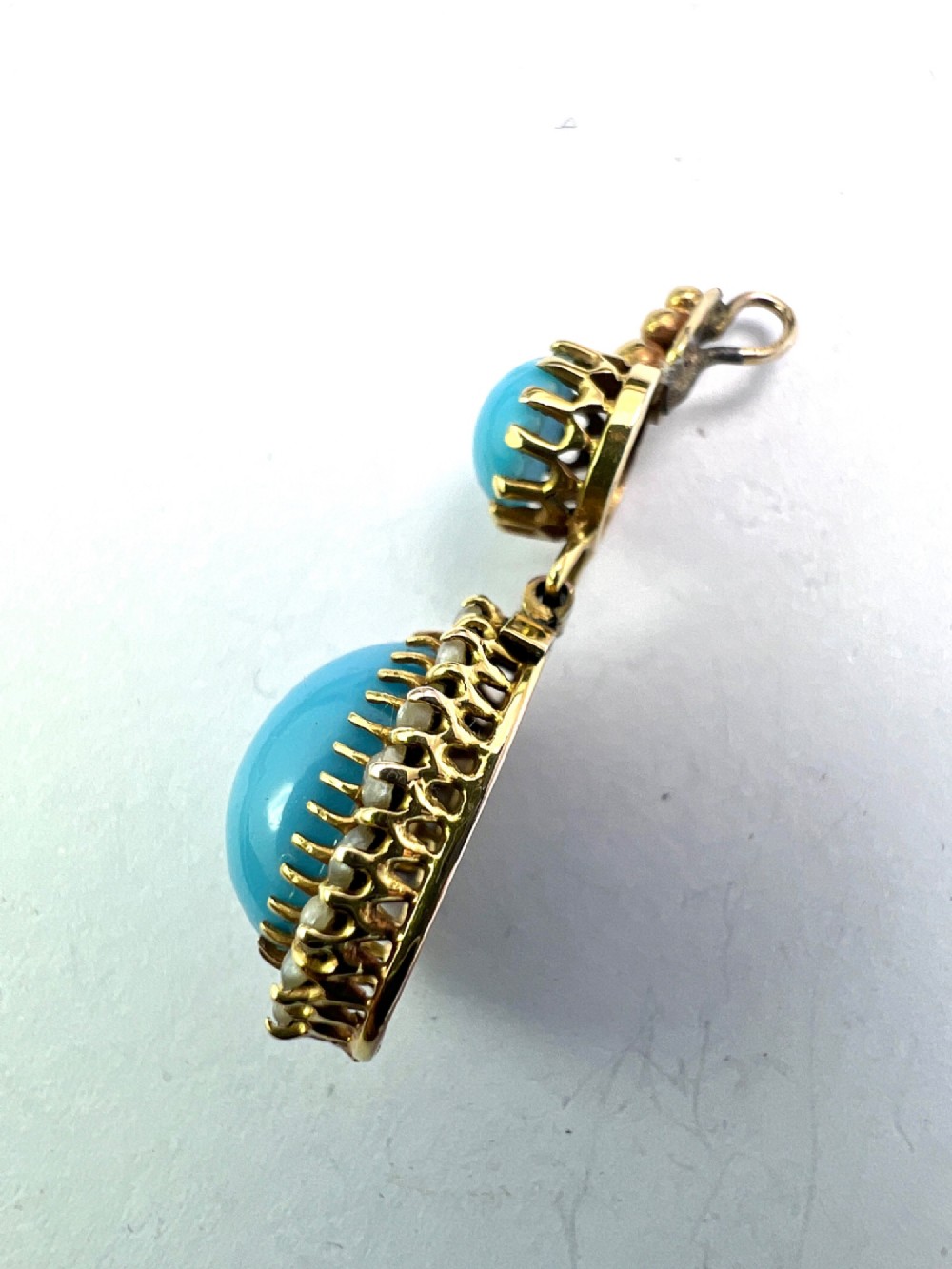 A Victorian yellow gold drop pendant featuring an oval turquoise cabochon framed by a seed pearl halo, hanging below a smaller round turquoise stone. View VI