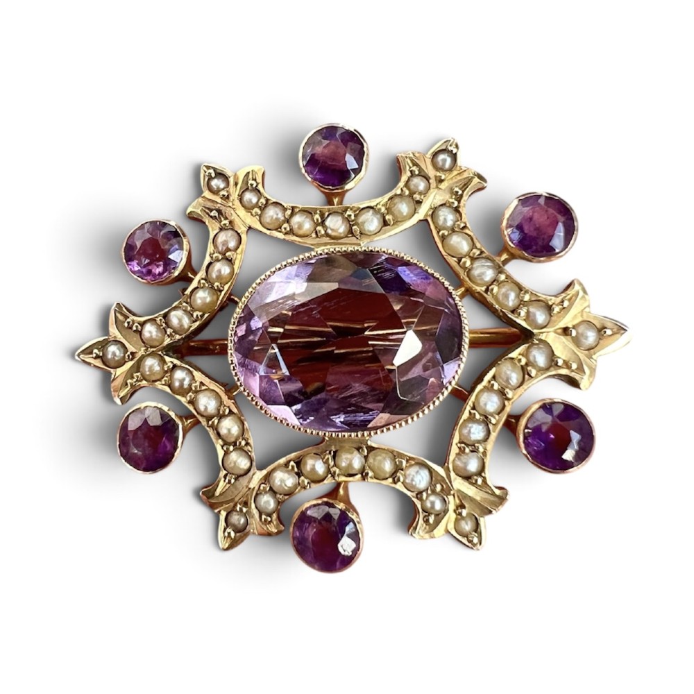 An Edwardian openwork 9ct gold brooch featuring a central oval faceted amethyst surrounded by split seed pearls and six outer round amethysts.