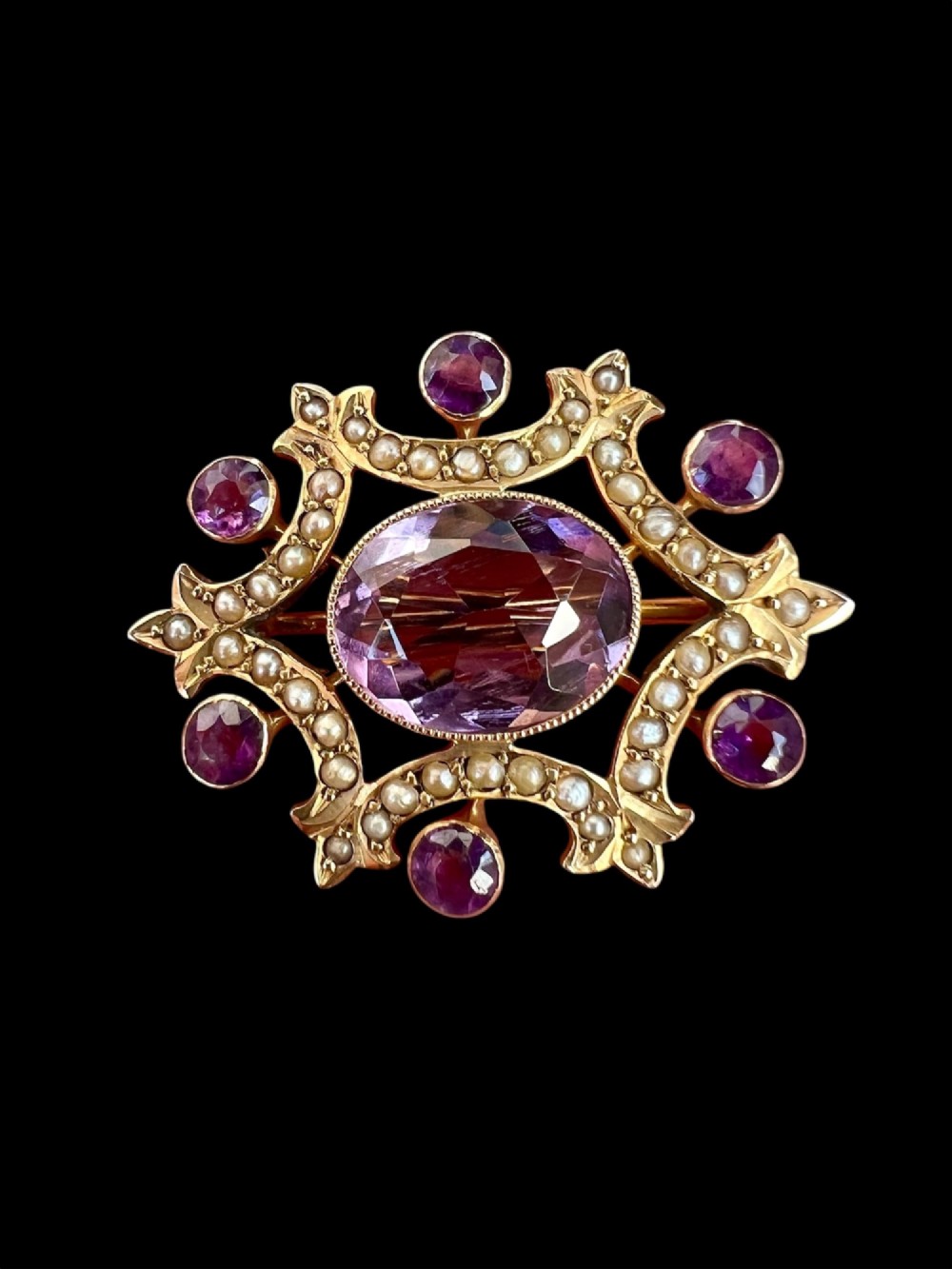 An Edwardian openwork 9ct gold brooch featuring a central oval faceted amethyst surrounded by split seed pearls and six outer round amethysts. View II